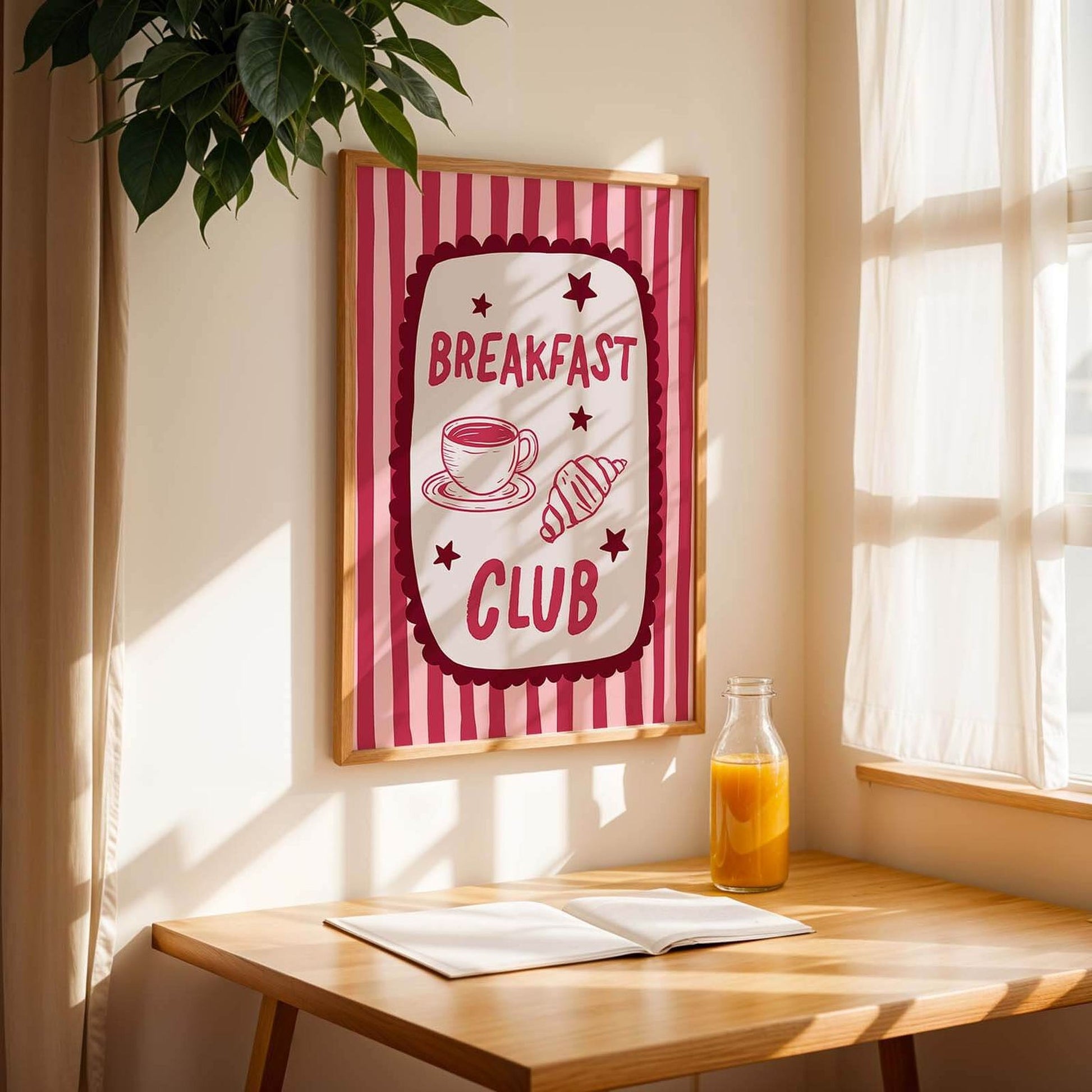 a framed poster with the text "BREAKFAST CLUB" hanging on a wall, accompanied by a cup and a bottle of orange juice on a wooden table.