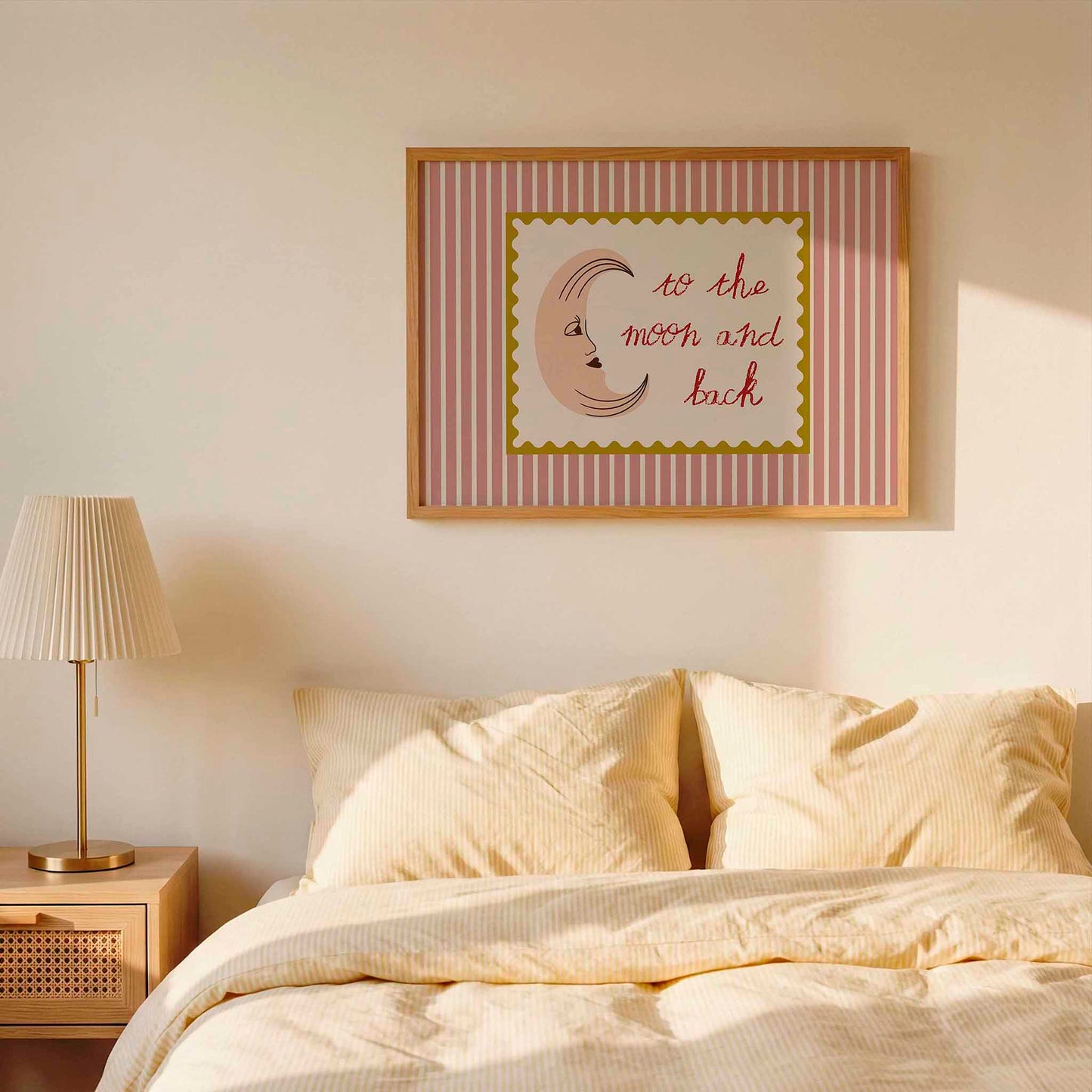 Framed artwork on a wall above a bed with striped bedding and a lamp.