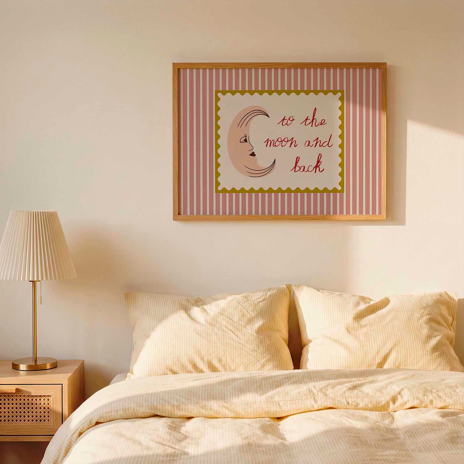 Framed artwork on a wall above a bed with striped bedding and a lamp.
