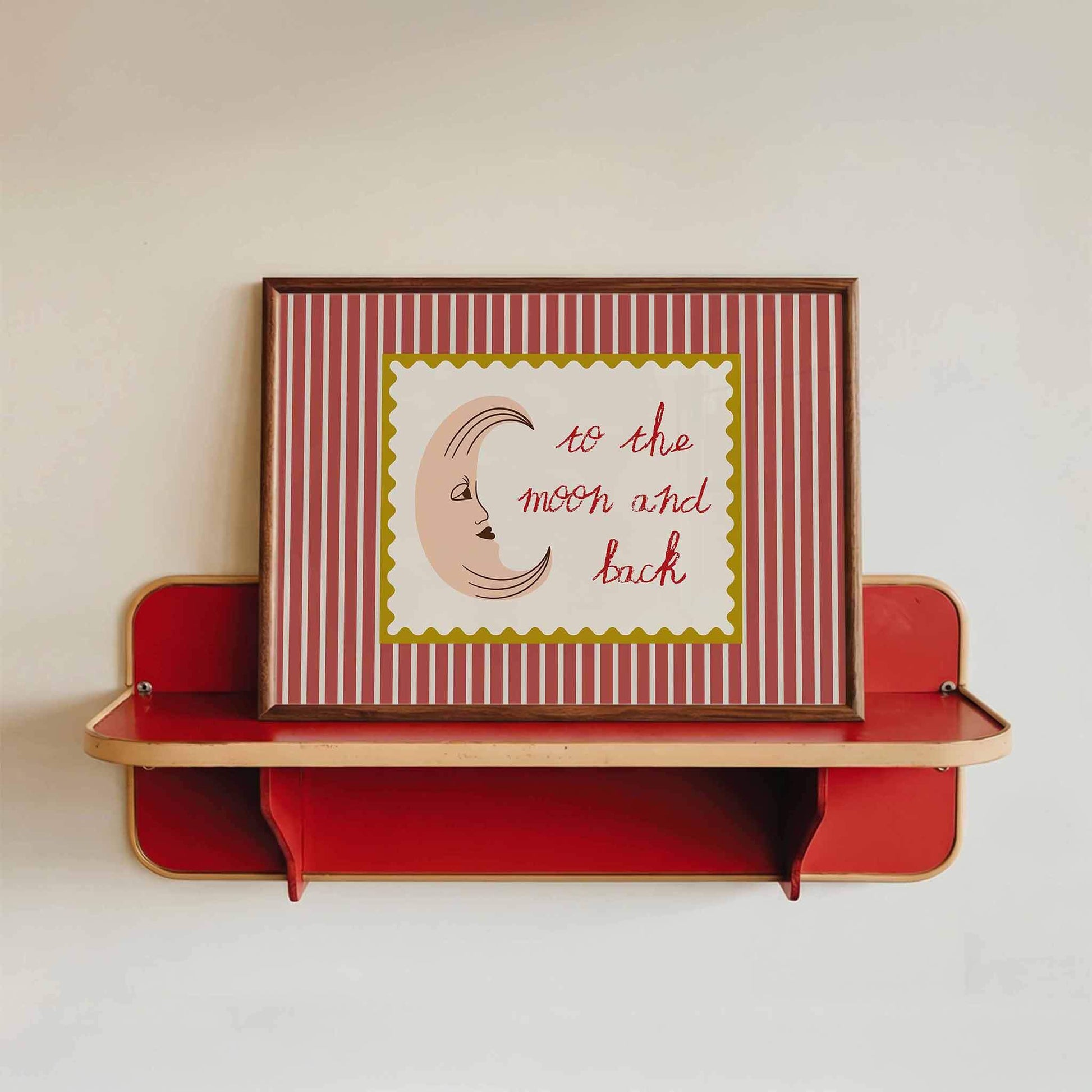 Framed artwork with 'to the moon and back' text on a red and white striped background, displayed on a red shelf.