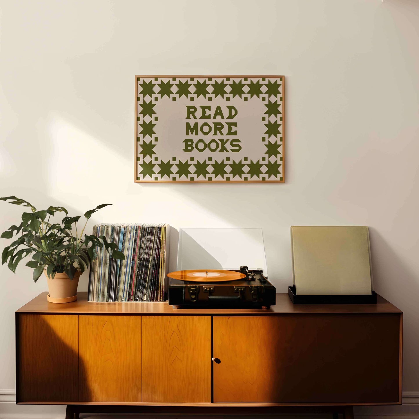Wooden sideboard with vinyl records, a plant, and a record player, with a motivational poster above.