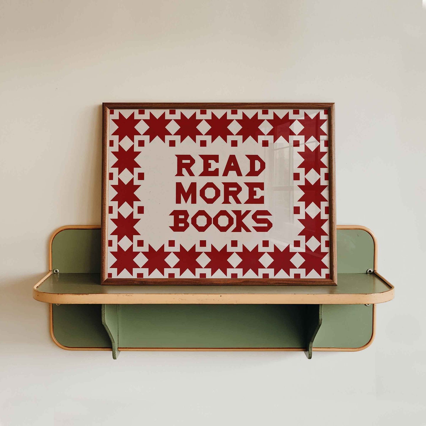 Decorative shelf with a framed quilt-style sign that says 'Read More Books' on a plain background.