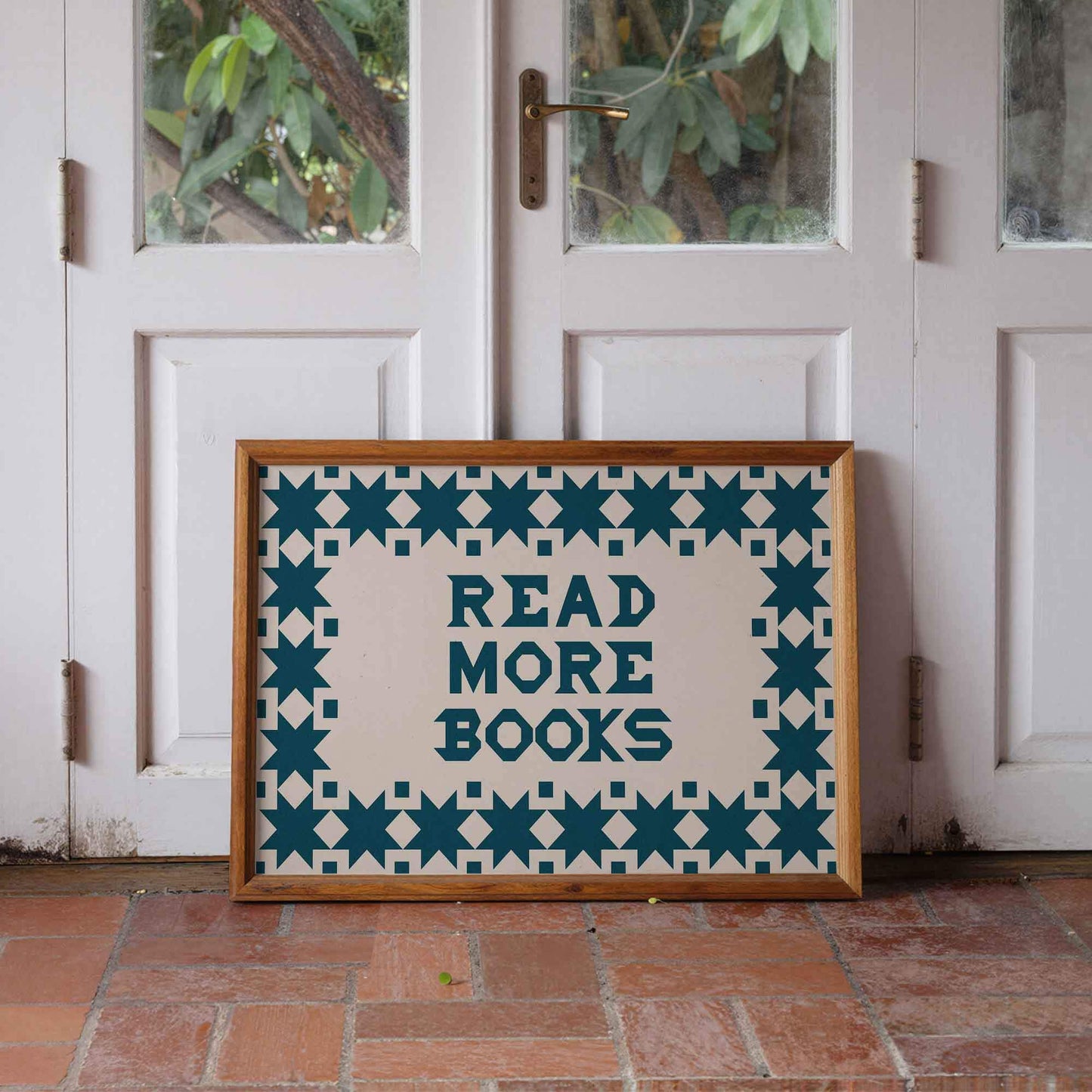 Framed poster with 'Read More Books' text on a tiled floor in front of a white door.
