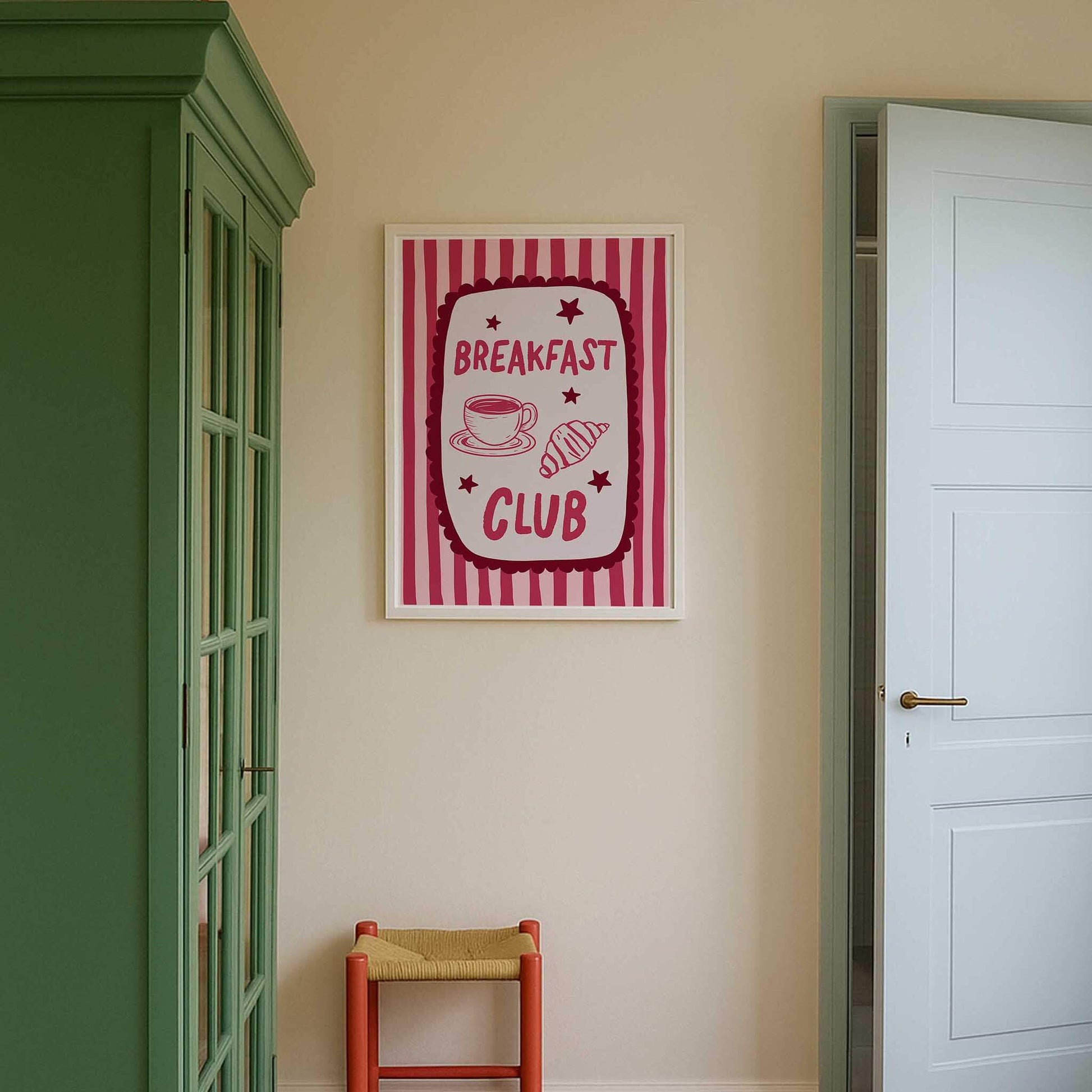 a framed sign with the text "BREAKFAST CLUB" hanging on a wall, accompanied by a red chair and a green cabinet.