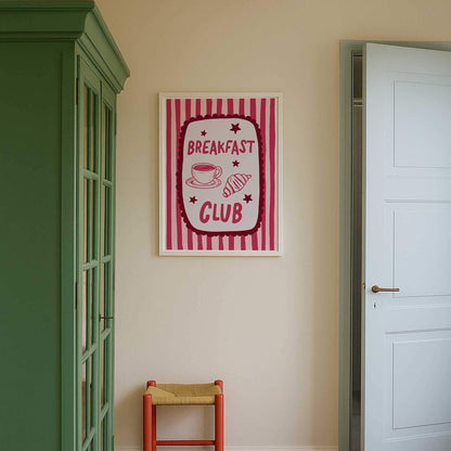 a framed sign with the text "BREAKFAST CLUB" hanging on a wall, accompanied by a red chair and a green cabinet.