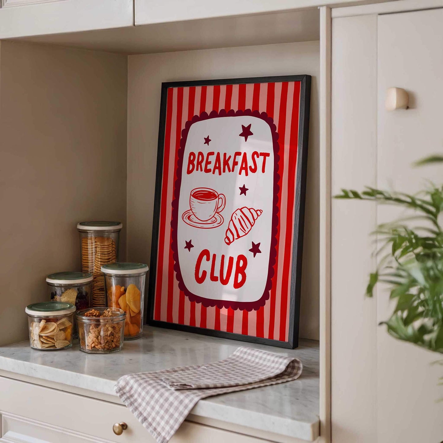 a framed sign that reads "BREAKFAST CLUB" with illustrations of a cup of coffee and pastries, placed on a kitchen counter.