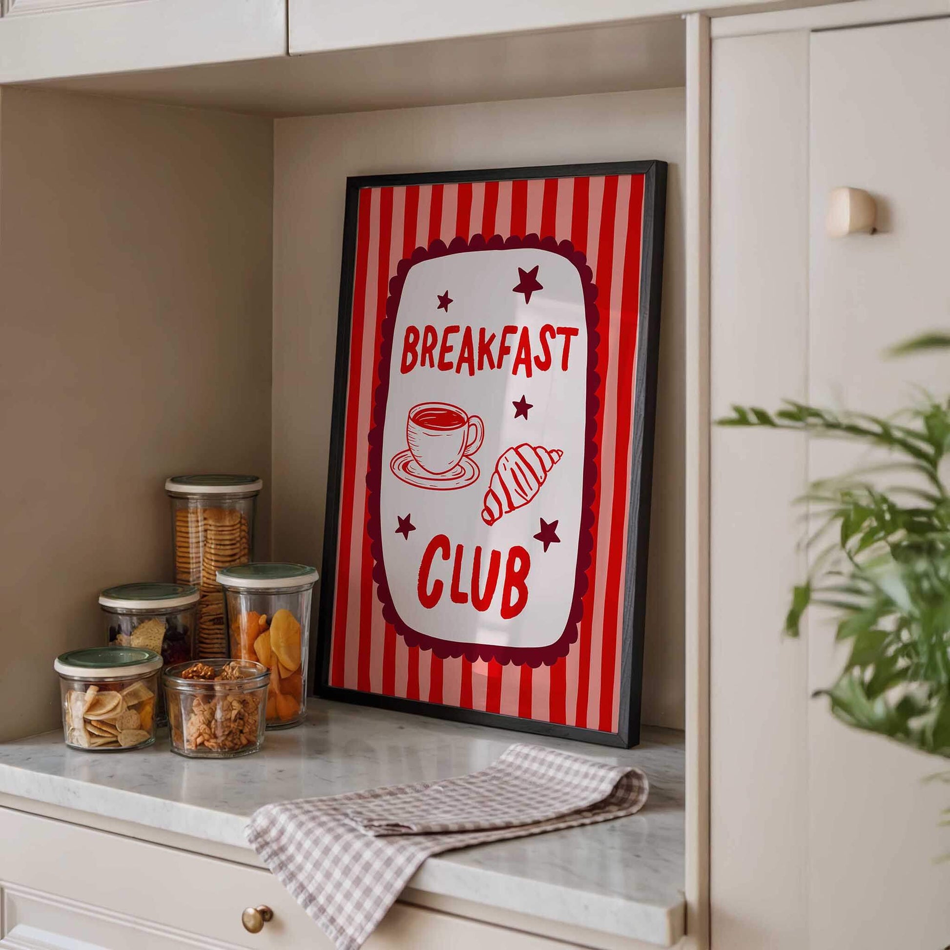a framed sign that reads "BREAKFAST CLUB" with illustrations of a cup of coffee and pastries, placed on a kitchen counter.