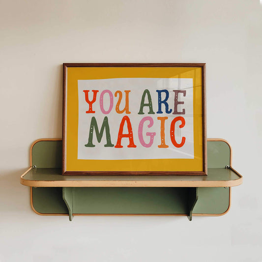 A framed poster with the text "YOU ARE MAGIC" displayed on a shelf.