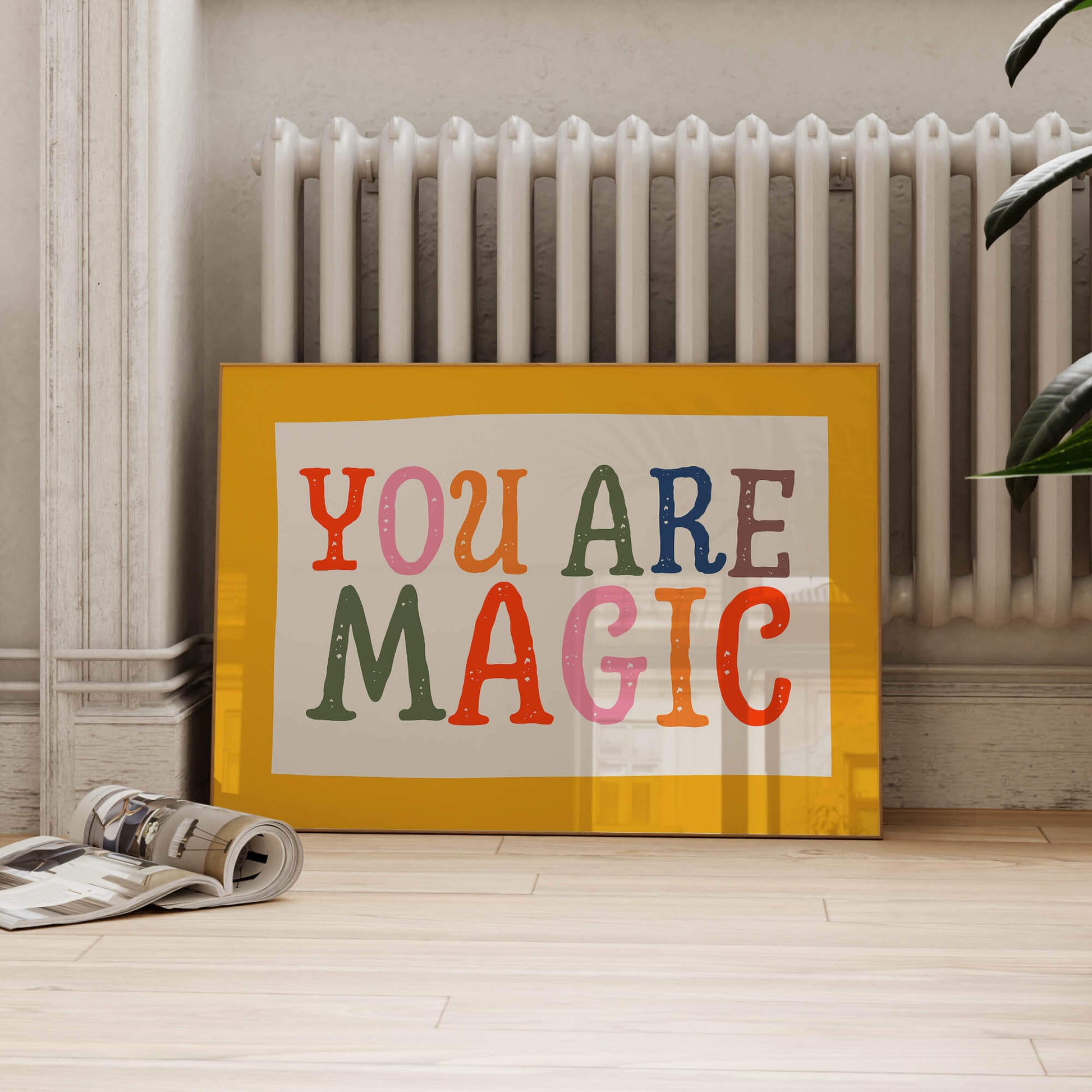 A framed poster with the text "YOU ARE MAGIC" is displayed on a wooden floor, with a white radiator visible in the background.