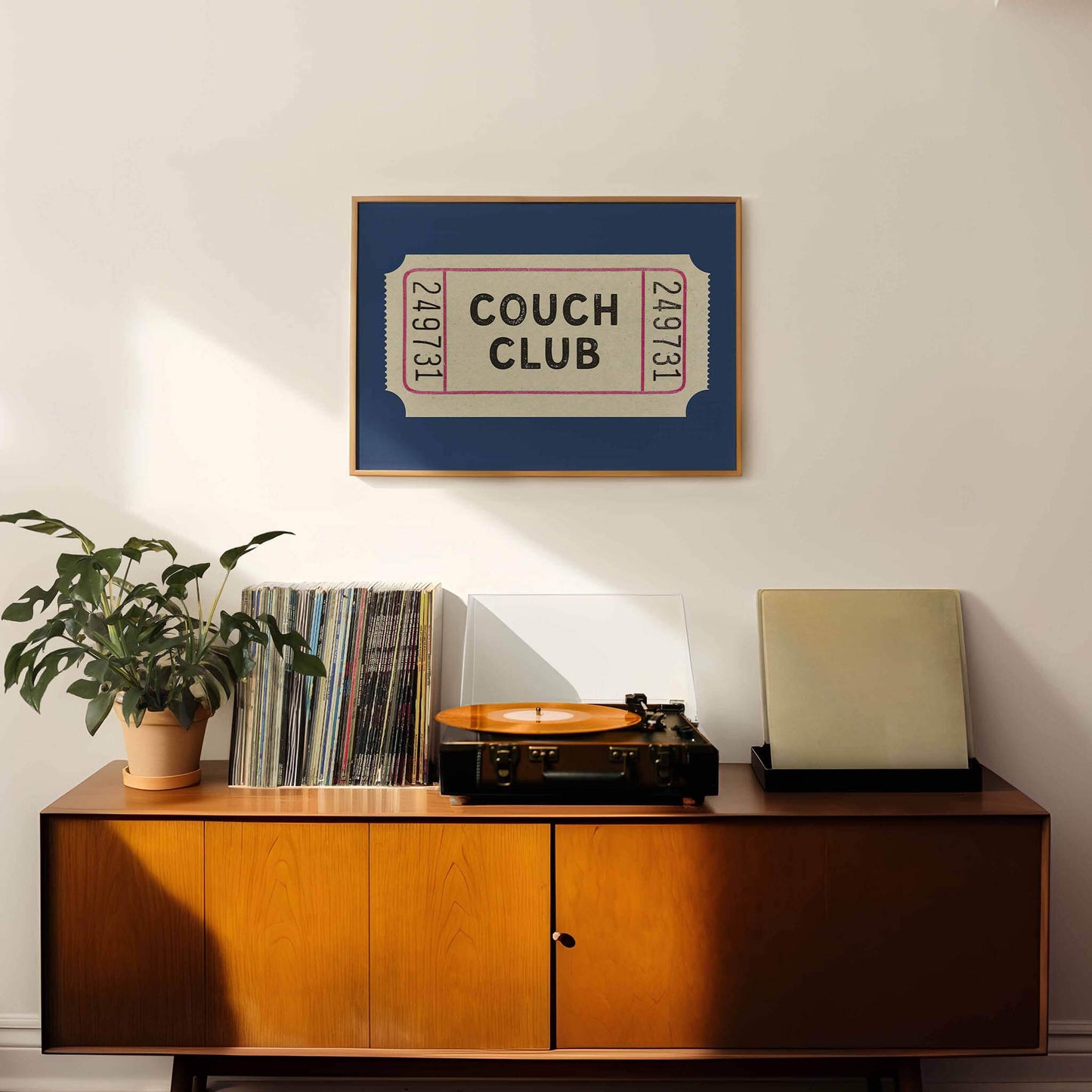 a wooden cabinet with a record player and a framed poster of a ticket for the "Couch Club" event.