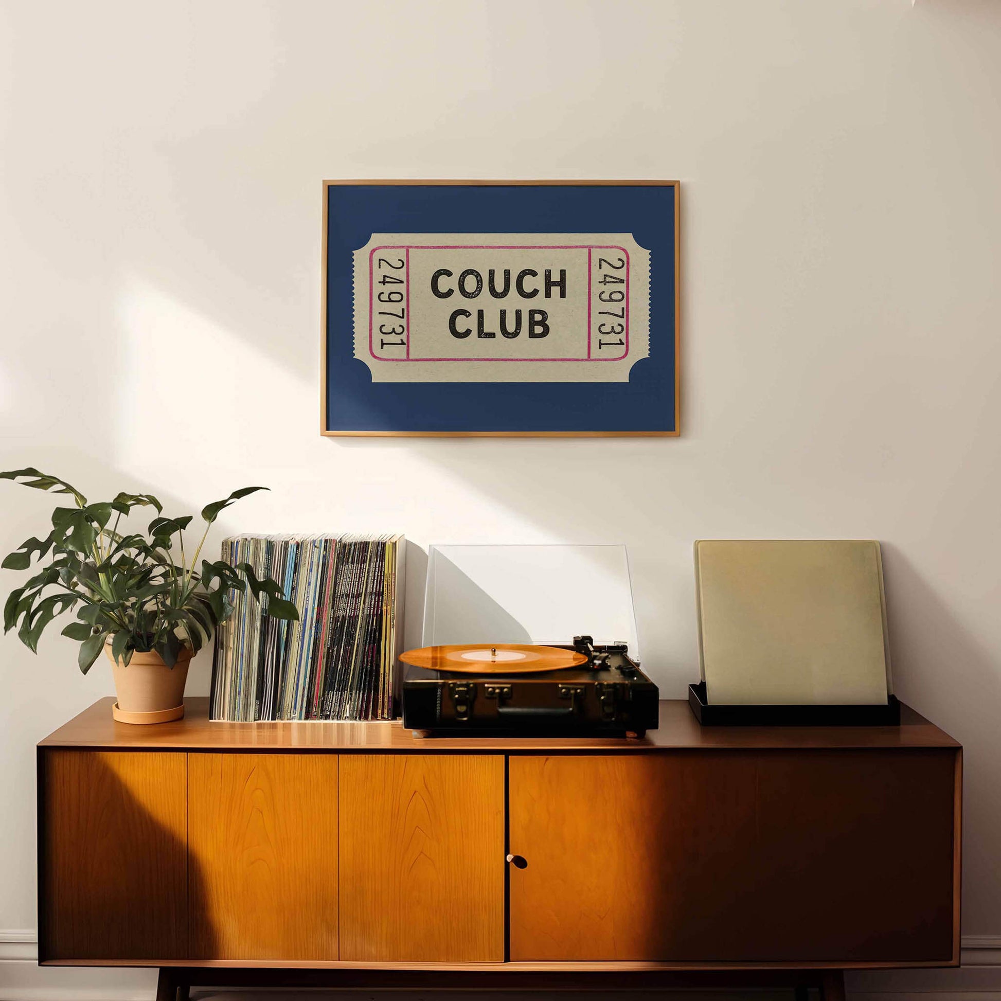 a wooden cabinet with a record player and a framed poster of a ticket for the "Couch Club" event.