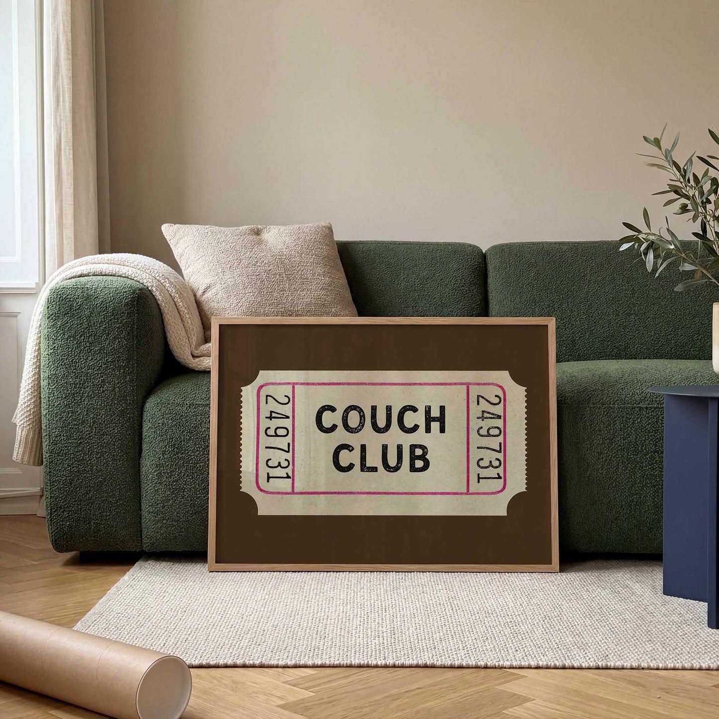 a framed ticket-style sign with the text "Couch Club" on a couch in a living room setting.
