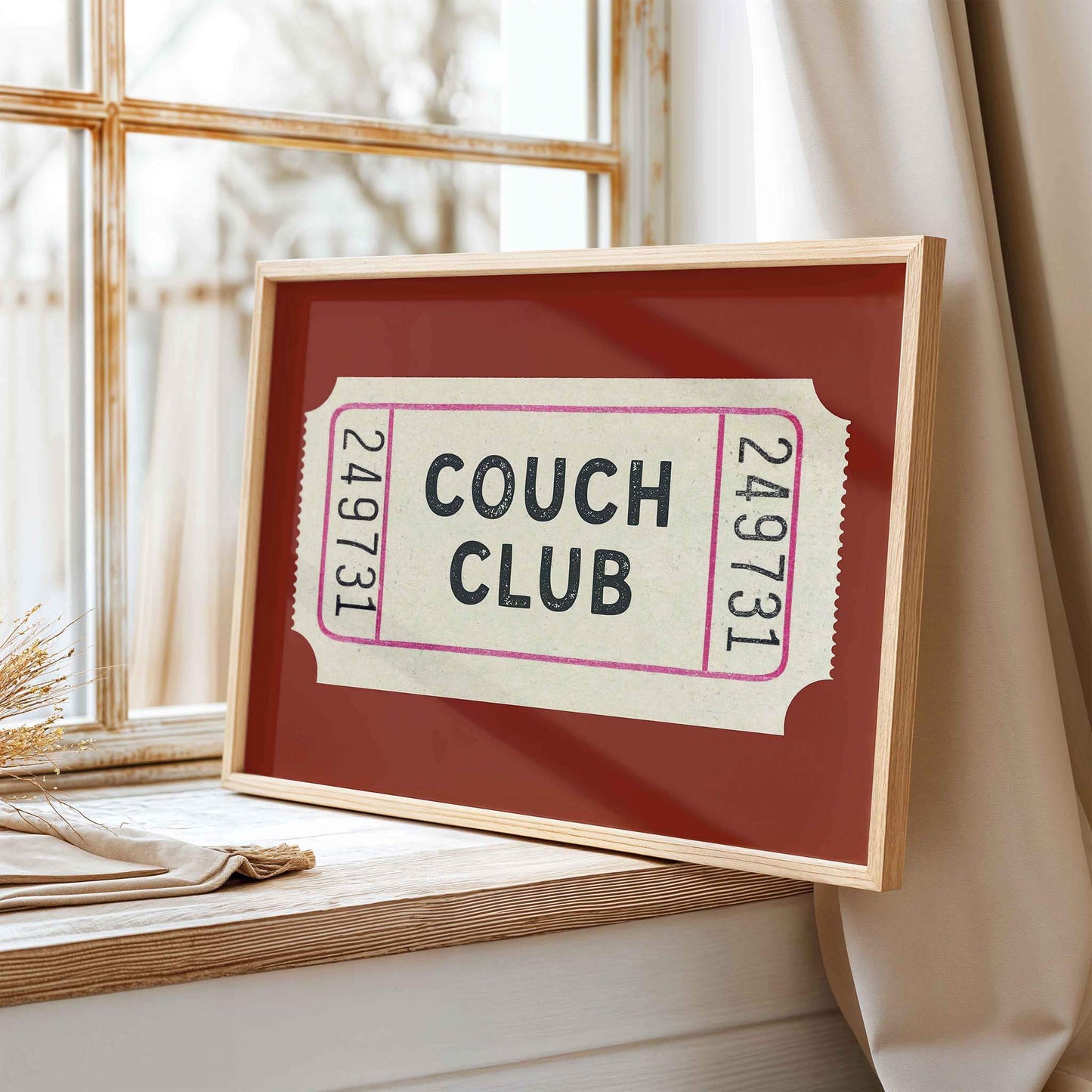A framed ticket-like sign with the text "Couch Club" displayed on it, placed on a windowsill.