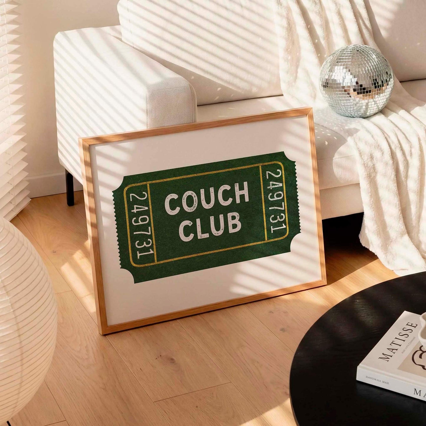 a framed poster with the text "Couch Club" on it, placed on a wooden floor in a living room setting.