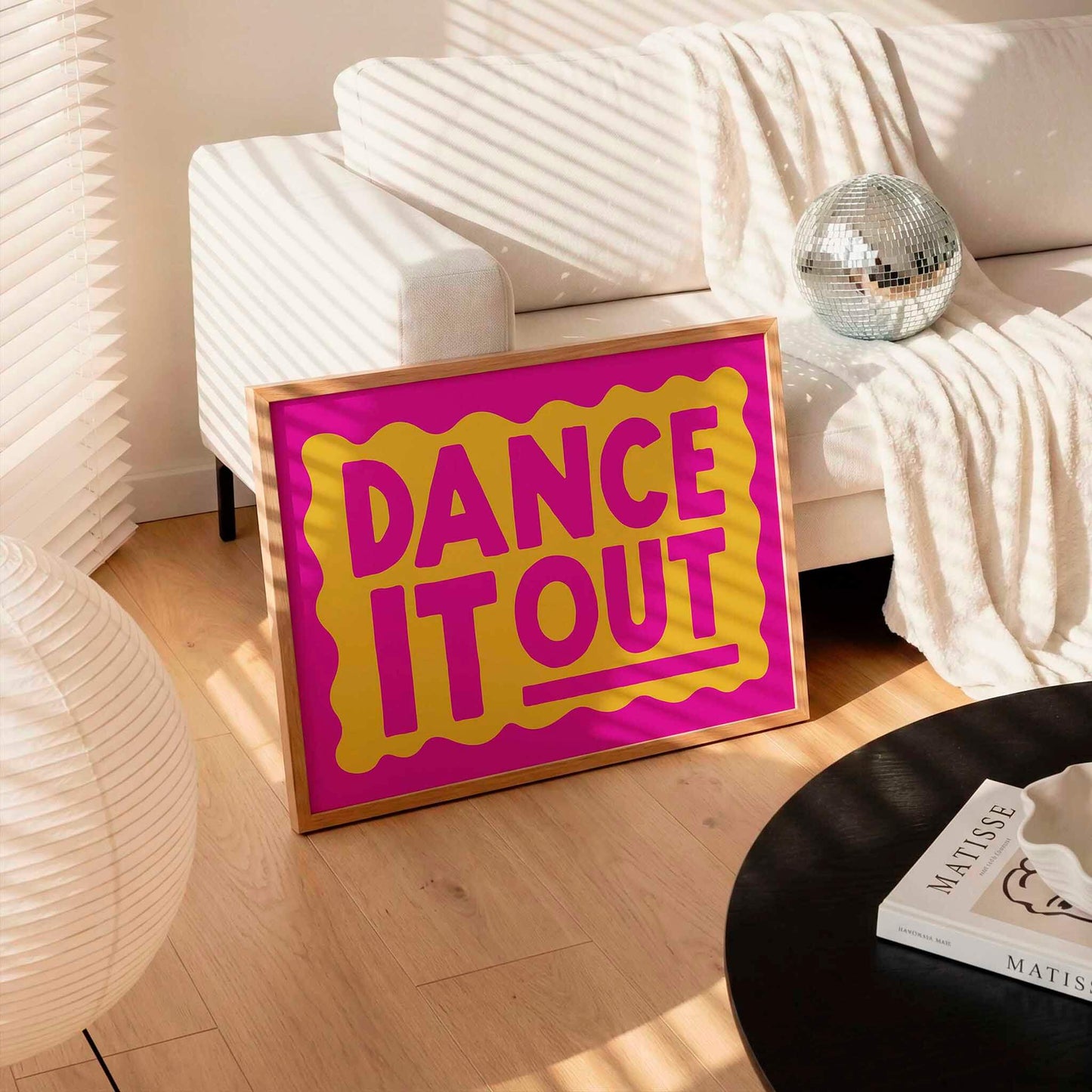 a large pink sign with the text "DANCE IT OUT" in yellow and orange letters, placed on a wooden floor in a living room setting.