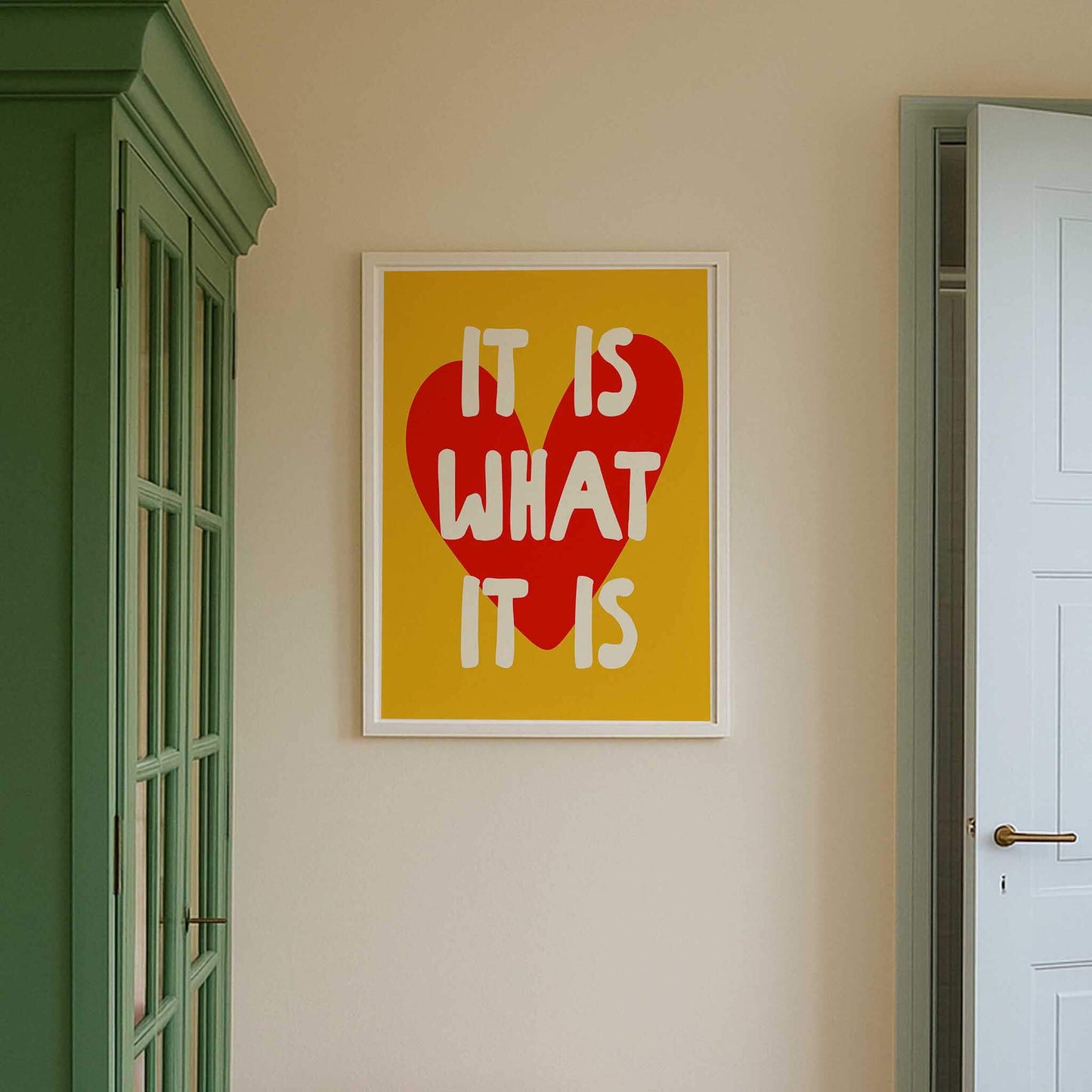 a framed poster with the text "IT IS WHAT IT IS" in bold letters, set against a yellow background with a red heart shape.
