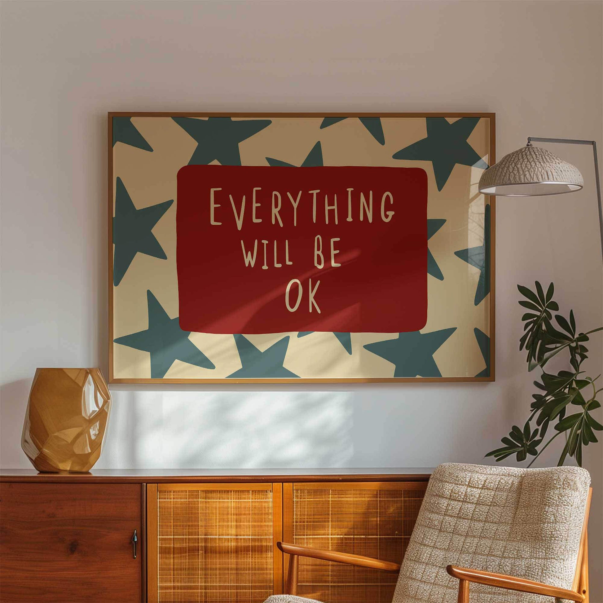 a framed poster with the text "Everything will be OK" displayed on a wall, accompanied by a wooden cabinet and a potted plant in the background.