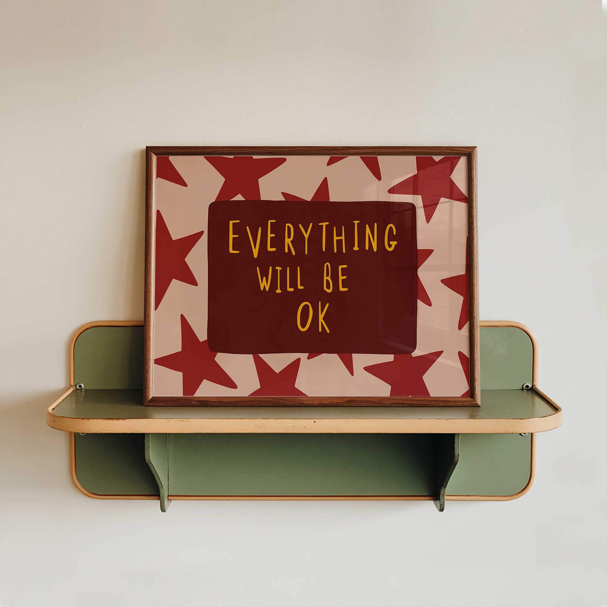 a framed poster with the text "EVERYTHING WILL BE OK" on it, displayed on a shelf against a white wall.