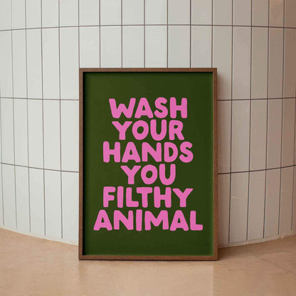 A framed poster with the text "WASH YOUR HANDS YOU FILTHY ANIMAL" in pink letters against a green background.