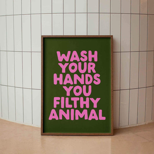 A framed poster with the text "WASH YOUR HANDS YOU FILTHY ANIMAL" in pink letters against a green background.