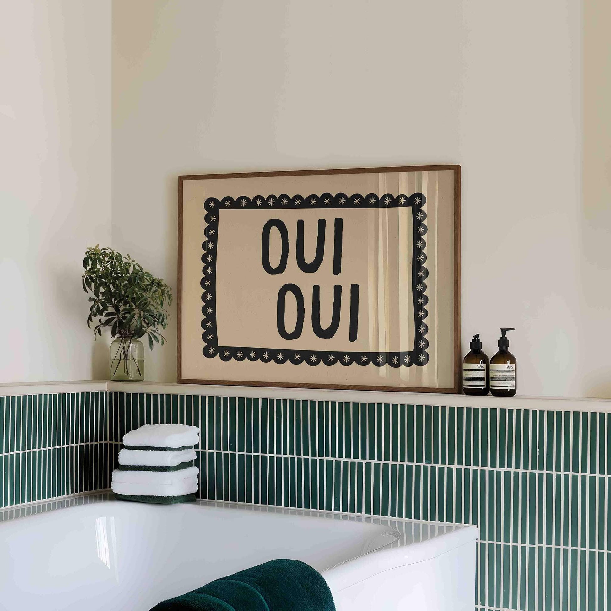 Bathroom with a framed picture saying 'OUI OUI', green tiles, and towels.