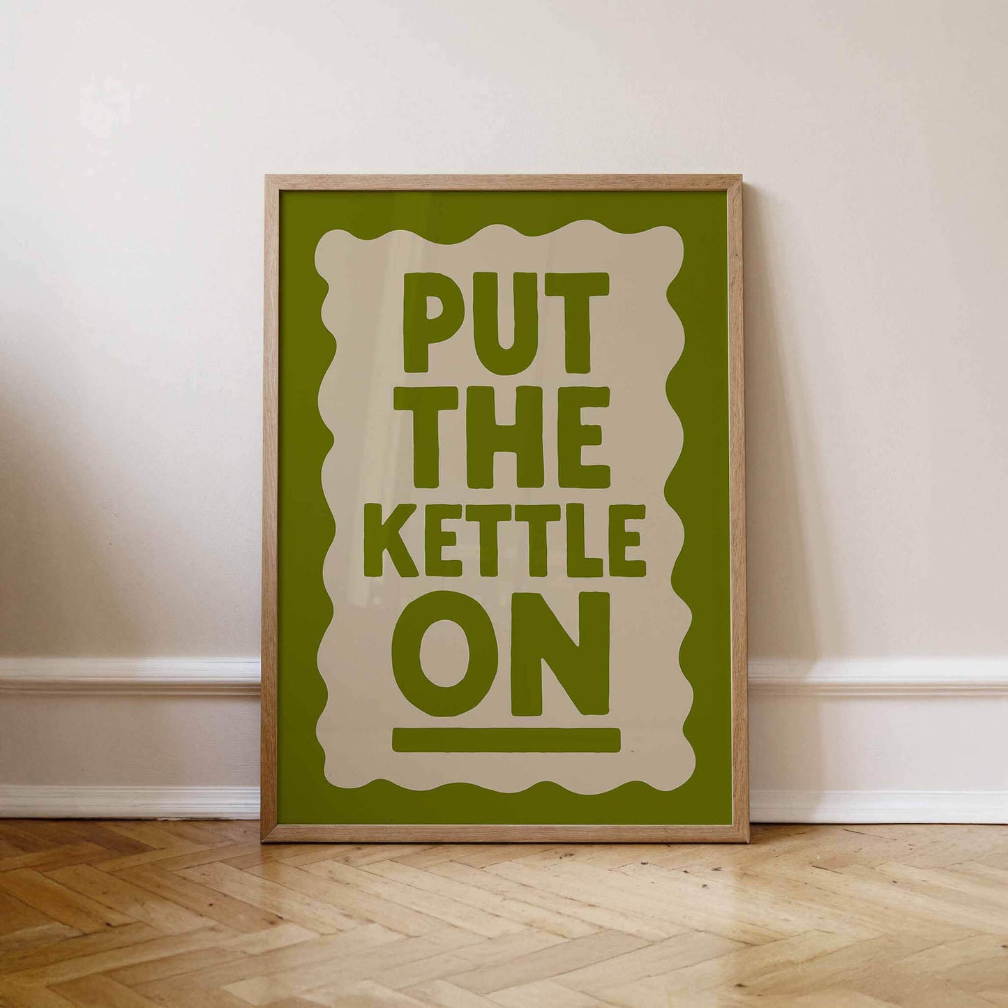 A framed poster with the text "PUT THE KETTLE ON" displayed on a white wall.