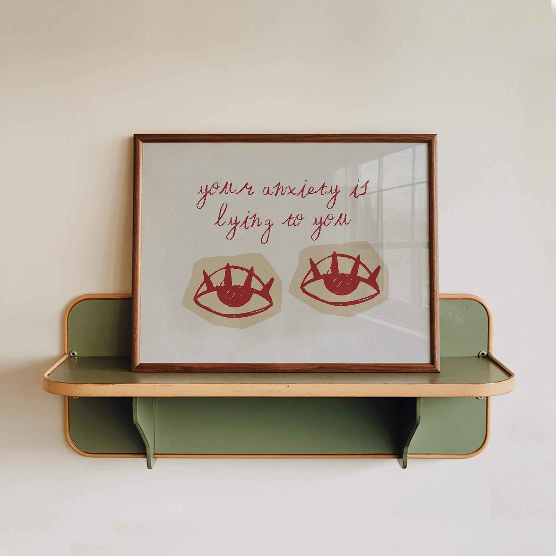 a framed artwork with a message about anxiety and lying, displayed on a shelf against a white wall.
