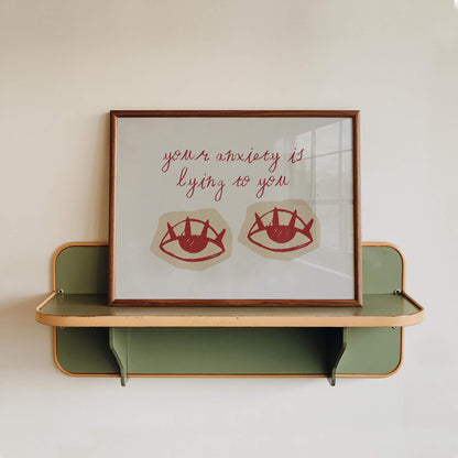 a framed artwork with a message about anxiety and lying, displayed on a shelf against a white wall.