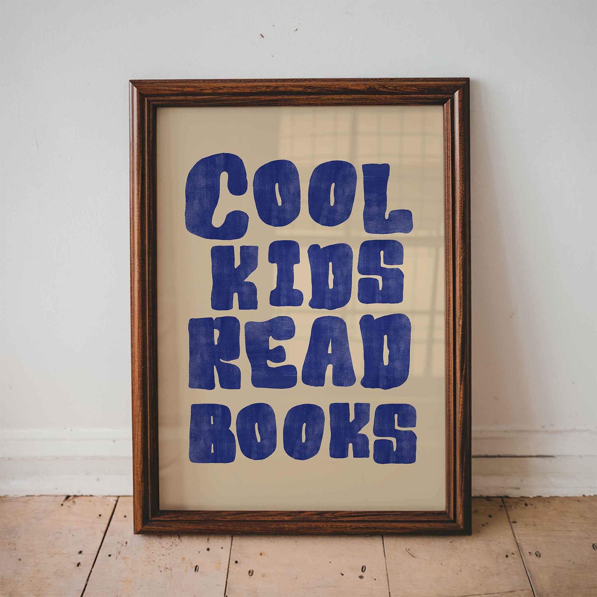 Framed poster with 'Cool kids read books' text on a wooden floor.