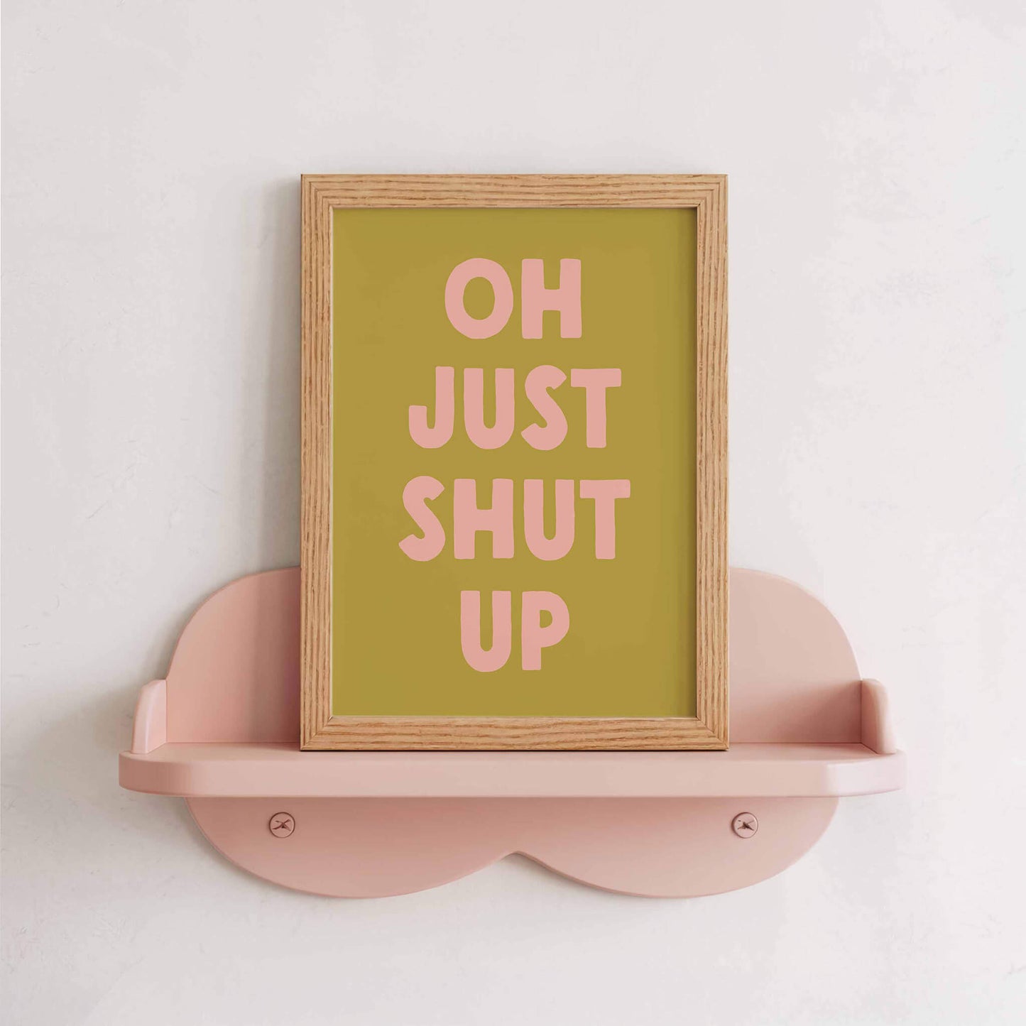 a framed poster with the text "OH JUST SHUT UP" displayed on a pink shelf.