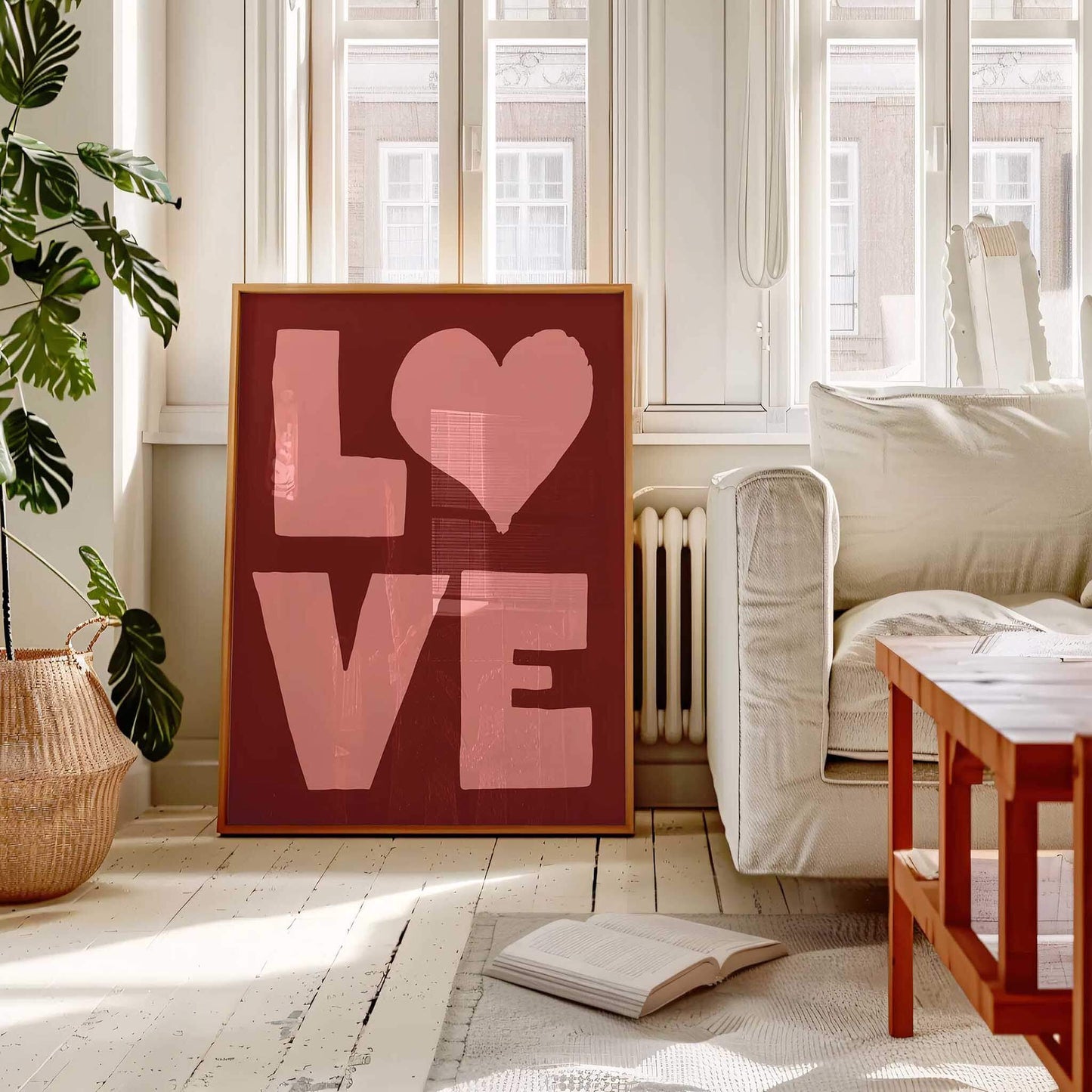 A large red poster with the word "LOVE" in bold pink letters is displayed in a bright, airy room with a white sofa, a wooden coffee table, and a potted plant.
