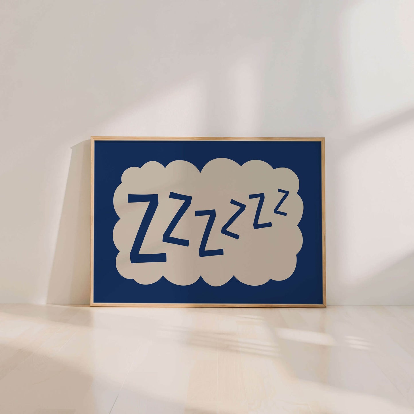 A framed poster with the word "zzzzzz" in a cloud-like shape, sitting on a wooden floor against a white wall.