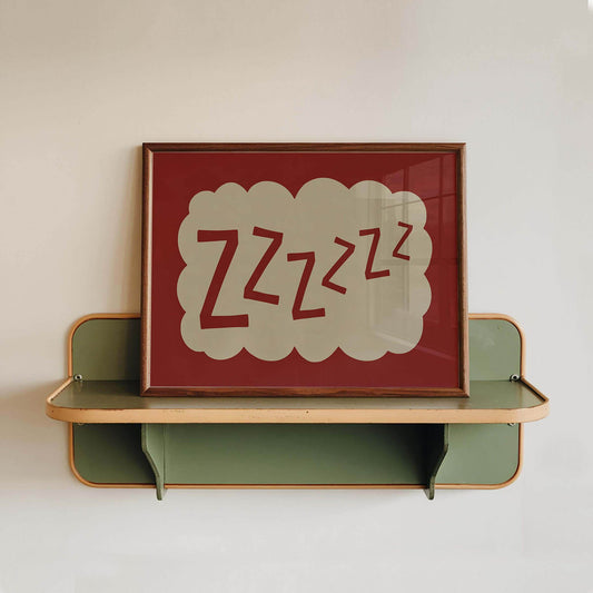 A framed picture with the text "zzzzzzzz" displayed on it, placed on a green shelf against a white wall.