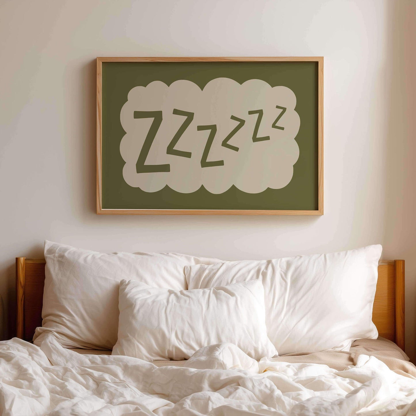 a bed with white pillows and a green framed picture hanging above it, depicting the word "zzzzzzzz" in a cloud-like shape.