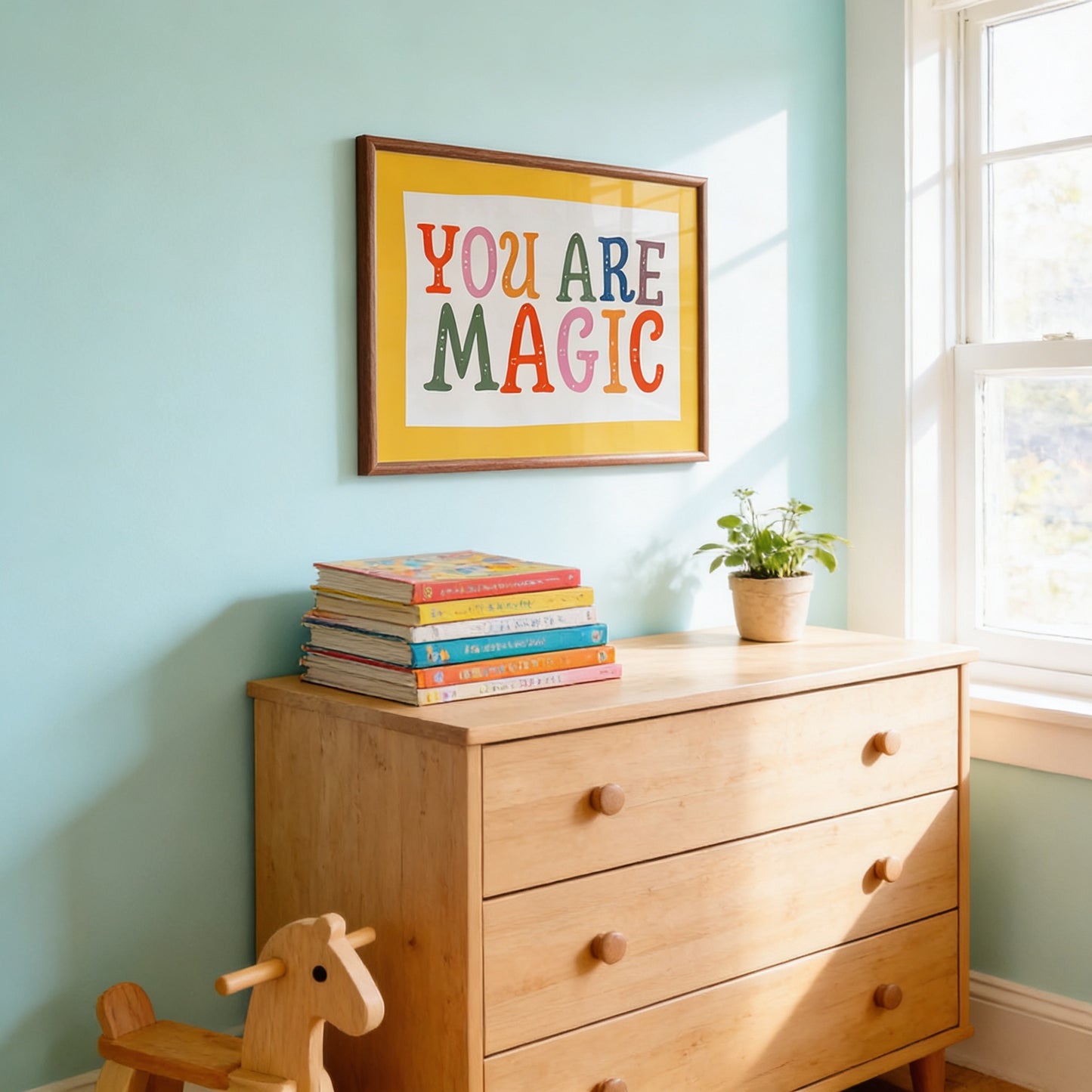 A wooden dresser with a stack of colorful books on top, a framed inspirational quote on the wall, and a small potted plant on the dresser.