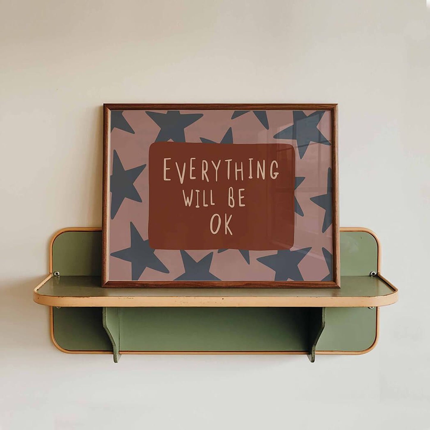 a framed poster with the text "EVERYTHING WILL BE OK" displayed on it, placed on a green shelf against a white wall.