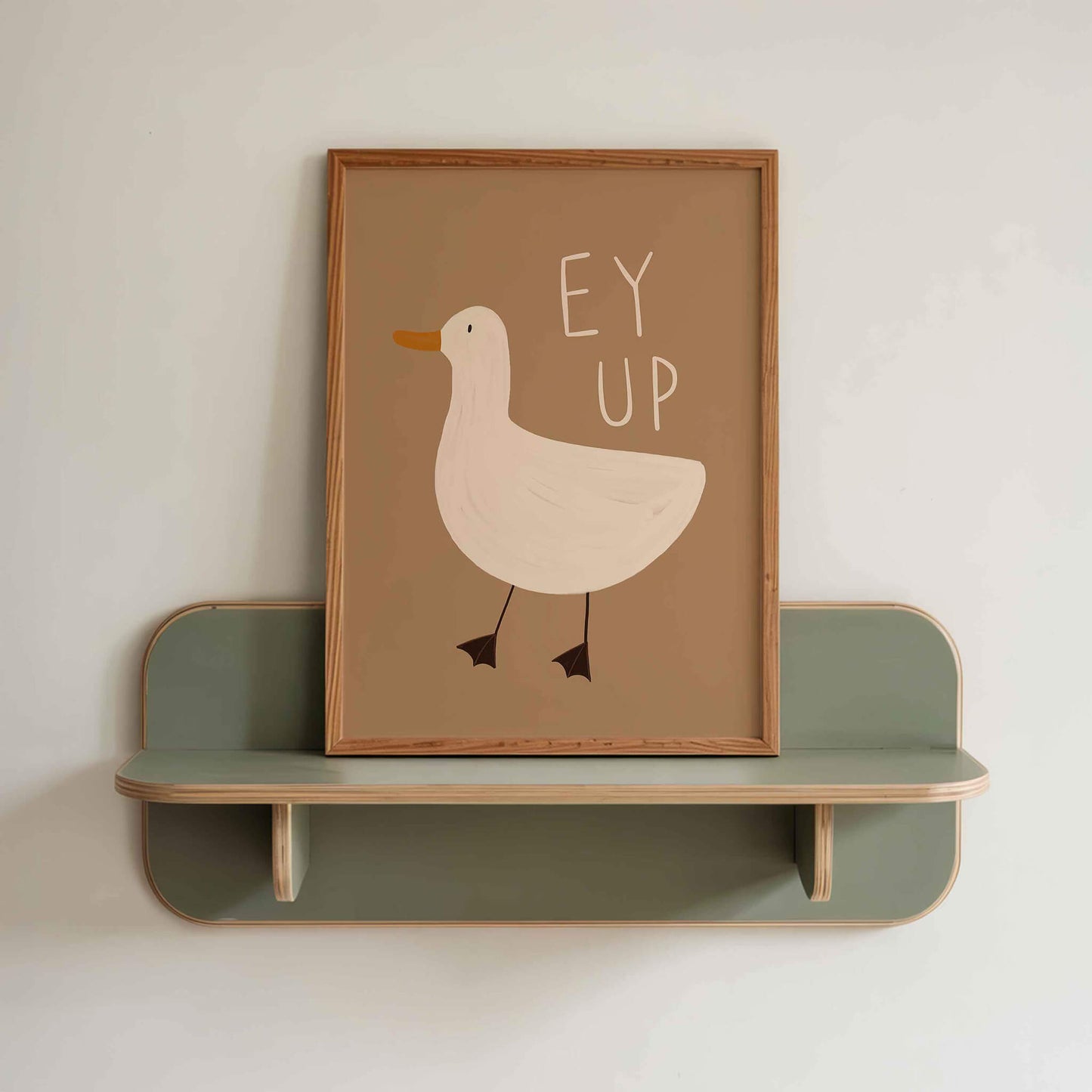 Framed, hand illustrated picture of a duck with 'EY UP' text on a green shelf against a white wall.