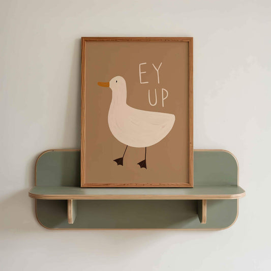 Framed, hand illustrated picture of a duck with 'EY UP' text on a green shelf against a white wall.