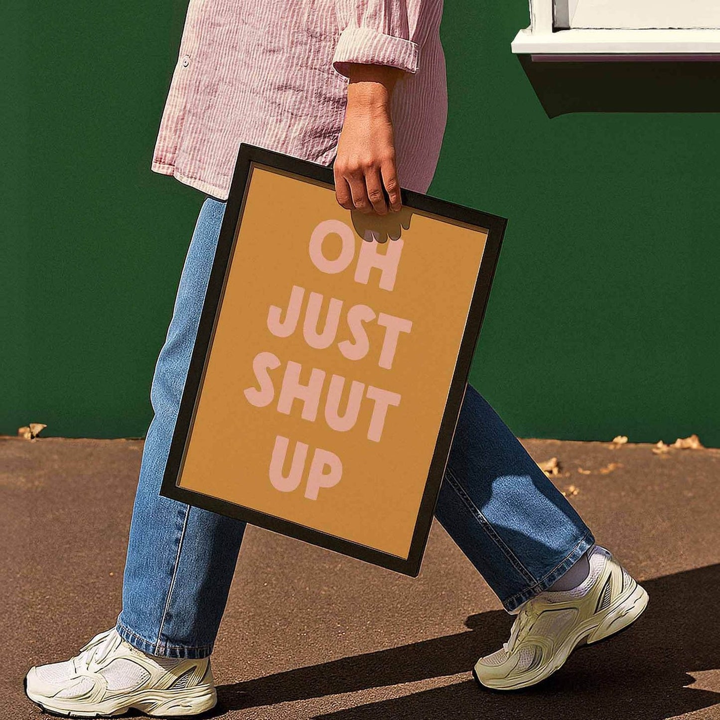 A person is walking while holding a framed sign that says "OH JUST SHUT UP".